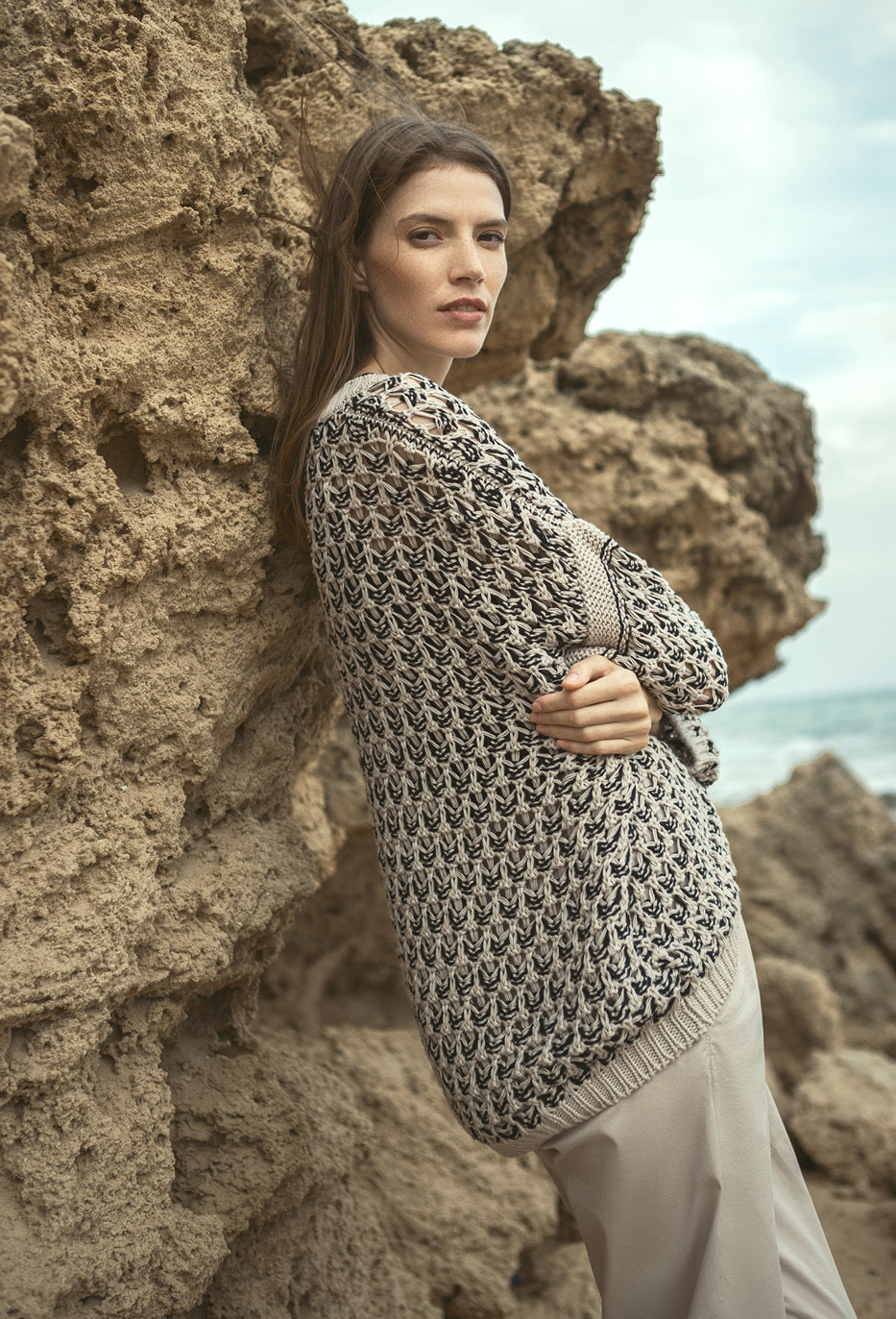 Stilvoll und ruhig präsentiert ein Model einen eleganten Strickpullover angelehnt an eine Felsenklippe.